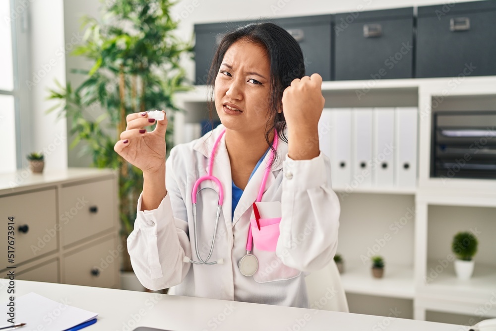 Sticker Young asian woman wearing doctor uniform and stethoscope annoyed and frustrated shouting with anger, yelling crazy with anger and hand raised