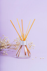 Glass bottle of reed diffuser and gypsophila blossom on lilac background. Closeup