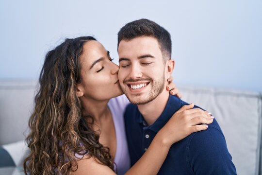 Young hispanic couple sitting on sofa hugging each other and kissing at home