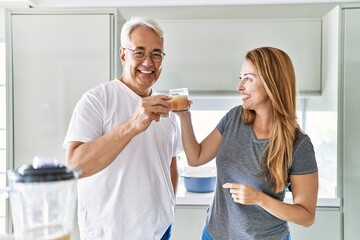 Middle age hispanic couple smiling happy drinking glass of smoothie at the kitchen.