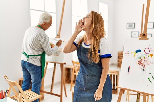 Hispanic woman wearing apron at art studio shouting and screaming loud to side with hand on mouth. communication concept.