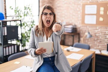 Young hispanic woman working at the office wearing glasses pointing displeased and frustrated to the camera, angry and furious with you