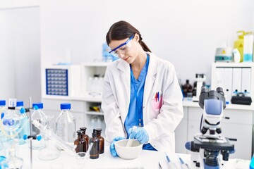 Fototapeta premium Young hispanic woman wearing scientist uniform working at laboratory
