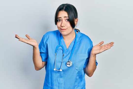 Beautiful hispanic woman wearing doctor uniform and stethoscope clueless and confused with open arms, no idea and doubtful face.