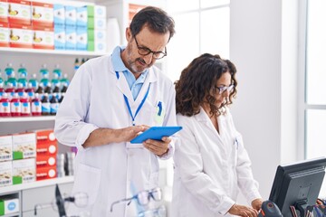 Man and woman pharmacists using touchpad and computer at pharmacy