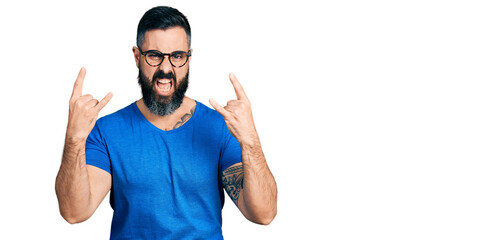 Hispanic man with beard wearing casual t shirt and glasses shouting with crazy expression doing...