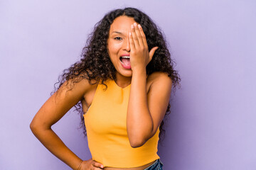 Young hispanic woman isolated on purple background having fun covering half of face with palm.