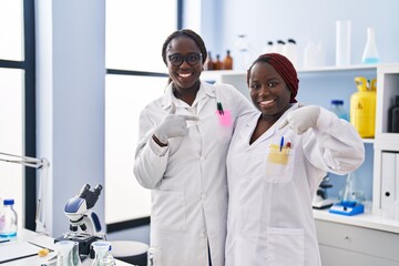 Two african women working at scientist laboratory pointing finger to one self smiling happy and proud