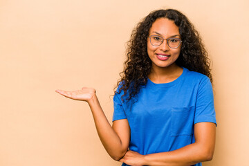 Young hispanic woman isolated on beige background showing a copy space on a palm and holding...