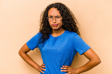 Young hispanic woman isolated on beige background frowning face in displeasure, keeps arms folded.