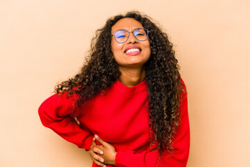 Young hispanic woman isolated on beige background having a liver pain, stomach ache.