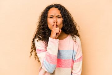 Young hispanic woman isolated on beige background keeping a secret or asking for silence.