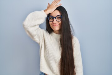 Young hispanic woman wearing casual sweater over blue background surprised with hand on head for...