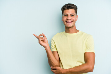 Young caucasian man isolated on blue background smiling cheerfully pointing with forefinger away.