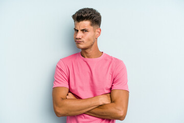 Young caucasian man isolated on blue background suspicious, uncertain, examining you.
