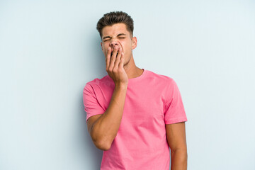 Young caucasian man isolated on blue background yawning showing a tired gesture covering mouth with hand.