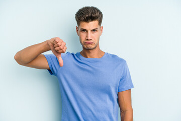 Young caucasian man isolated on blue background showing a dislike gesture, thumbs down....