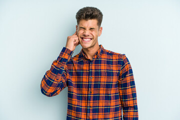 Fototapeta premium Young caucasian man isolated on blue background covering ears with fingers, stressed and desperate by a loudly ambient.