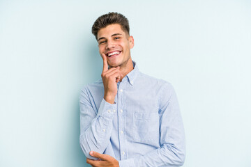 Young caucasian man isolated on blue background smiling happy and confident, touching chin with hand.