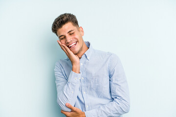 Young caucasian man isolated on blue background laughs happily and has fun keeping hands on stomach.