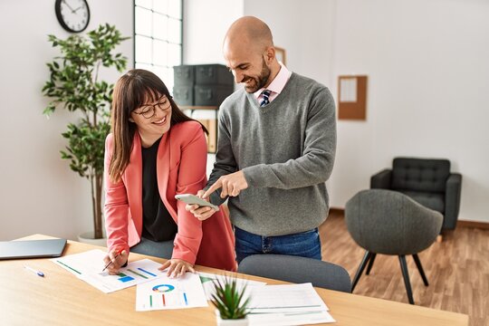 Two hispanic business workers smiling happy working using smartphone at the office.
