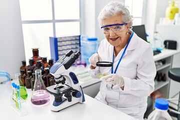 Senior grey-haired woman wearing scientist uniform using loupe at laboratory