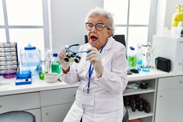 Senior woman with grey hair working at scientist laboratory using magnifying glasses celebrating crazy and amazed for success with open eyes screaming excited.