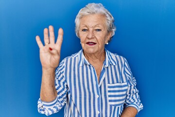 Senior woman with grey hair standing over blue background showing and pointing up with fingers number four while smiling confident and happy.
