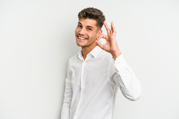 Young caucasian man isolated on white background winks an eye and holds an okay gesture with hand.