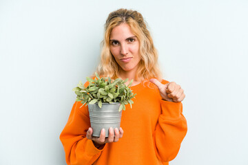 Young caucasian woman holding a plant isolated on blue background feels proud and self confident, example to follow.