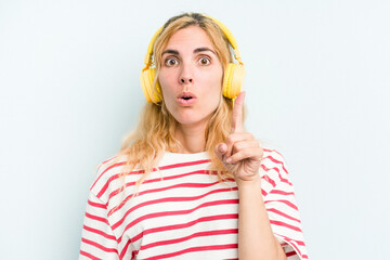 Young caucasian woman listening to music isolated on blue background having some great idea, concept of creativity.