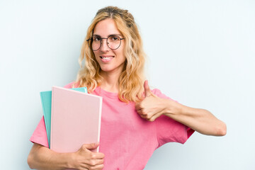 Fototapeta premium Young student caucasian woman holding books isolated on blue background smiling and raising thumb up