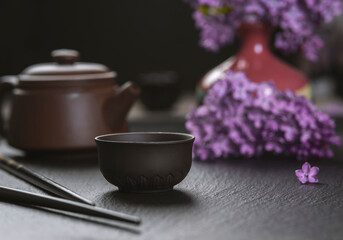Brown ceramic asian teapot , tea cups and chopsticks on background of purple flowers. Japanese food...