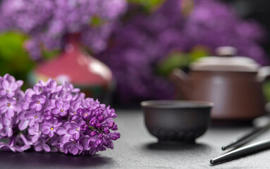 Obraz na płótnie Canvas Brown ceramic asian teapot , tea cups and chopsticks on background of purple flowers. Japanese food concept