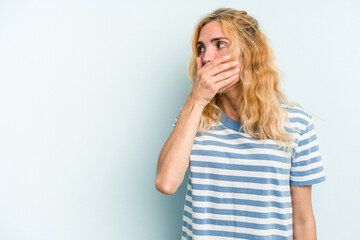 Young caucasian woman isolated on blue background thoughtful looking to a copy space covering mouth with hand.