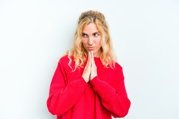 Young caucasian woman isolated on blue background praying, showing devotion, religious person looking for divine inspiration.