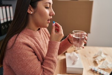 Young hispanic woman ecommerce business worker taking pill at office