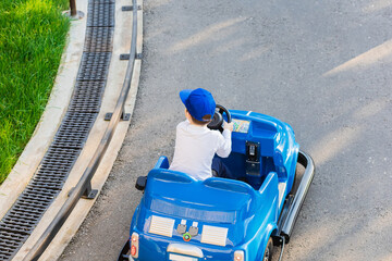 A boy in a blue cap drives a blue miniature children's car along a park road. Children's circuit in the amusement park. Karting for kids