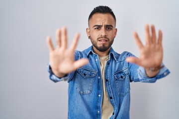 Fototapeta premium Young hispanic man standing over isolated background doing stop gesture with hands palms, angry and frustration expression