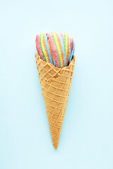 Colorful sour jelly candies in sugar sprinkles in an ice cream cone on a light blue background