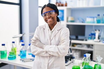 African american woman working at scientist laboratory happy face smiling with crossed arms looking...