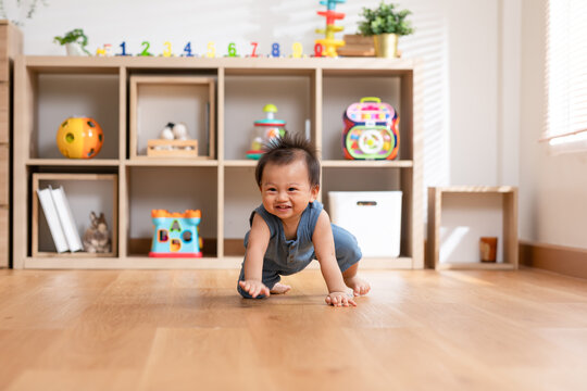 Healthy asian baby toddler crawling on floor to learn to crawl indoors. Adorable baby keeping her belly and legs down on the floor to belly crawl fun and happiness at home