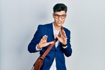 Young hispanic man wearing business clothes disgusted expression, displeased and fearful doing disgust face because aversion reaction. with hands raised