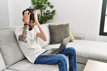 Fototapeta premium Hispanic man with beard sitting on the sofa suffering from headache desperate and stressed because pain and migraine. hands on head.