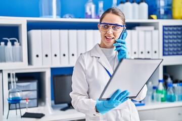 Young woman scientist talking on the smartphone reading document at laboratory