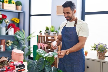 Young hispanic man florist smiling confident watering plant at florist