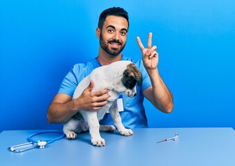 Handsome hispanic veterinary man with beard checking dog health smiling looking to the camera...