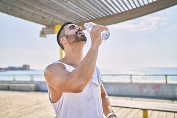 Hispanic sports man wearing workout style drinking water to stay hydrated outdoors on a sunny day