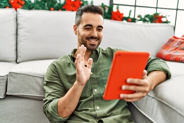 Young hispanic man having video call sitting on the floor by christmas decor at home