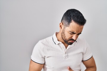 Young hispanic man with beard wearing casual clothes over white background with hand on stomach because indigestion, painful illness feeling unwell. ache concept.